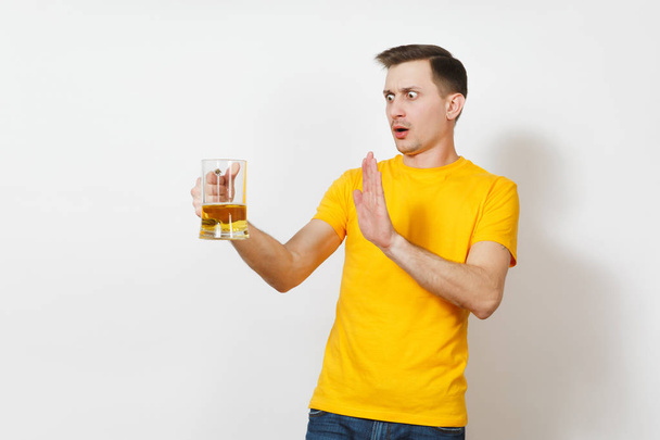 Young European serious handsome man in yellow t-shirt refuse pint mug of beer, show stop drink alcohol gesture with hand isolated on white background. Sport teenager health, healthy lifestyle concept. - Photo, Image