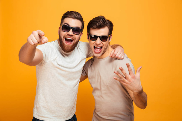 Two happy men friends in casual t-shirts and sunglasses having f - Photo, Image