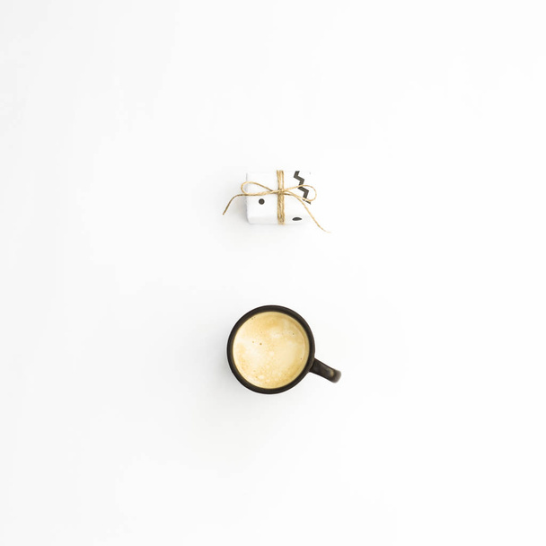 Uma xícara de café e um pequeno presente minimalista em um fundo branco. Deitado plano, vista superior
 - Foto, Imagem
