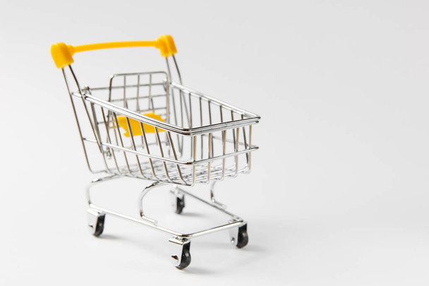 Close up of supermarket grocery push cart for shopping with black wheels and yellow plastic elements on handle isolated on white background. Concept of shopping. Copy space for advertisement - Foto, afbeelding