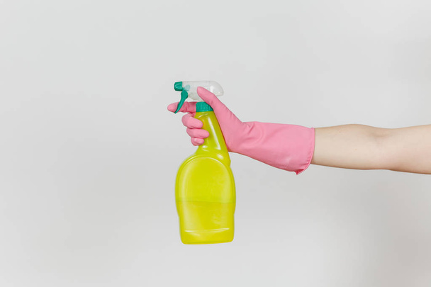 Primer plano de la mano femenina en guantes de color rosa haga clic en botella de aerosol amarillo con líquido más limpio con lugar para el texto aislado sobre fondo blanco. Concepto de artículos de limpieza. Copiar espacio para publicidad
 - Foto, Imagen