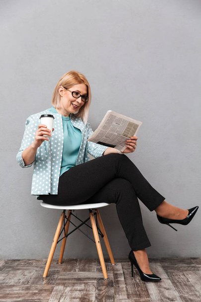 Cheerful business woman drinking coffee reading newspaper. - Foto, Imagen