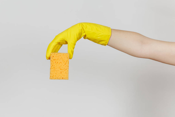 El primer plano de la mano femenina en guantes amarillos horizontales sostiene la esponja amarillo-naranja para limpiar y lavar los platos aislados sobre fondo blanco. Concepto de artículos de limpieza. Copiar espacio para publicidad
 - Foto, Imagen