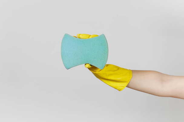 El primer plano de la mano femenina en guantes amarillos horizontales sostiene una gran esponja azul para limpiar y lavar los platos aislados sobre fondo blanco. Concepto de artículos de limpieza. Copiar espacio para publicidad
 - Foto, Imagen