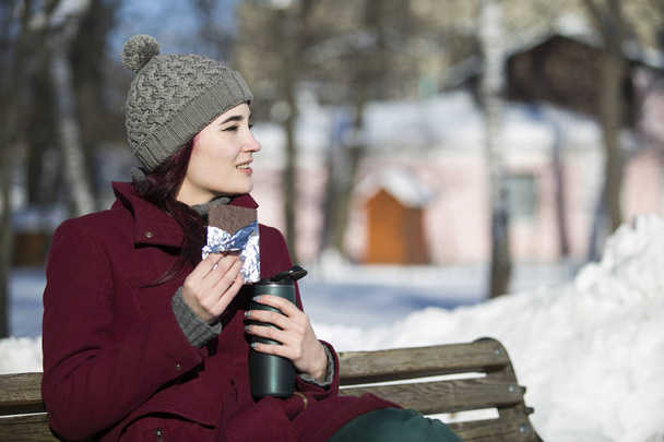 w 冬の公園のベンチに座っている少女のコートに、帽子 - 写真・画像
