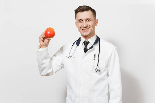 Smiling handsome young doctor man isolated on white background. Male doctor in medical uniform stethoscope holding red apple. Healthcare personnel health medicine concept. Proper nutrition. Copy space - Photo, Image