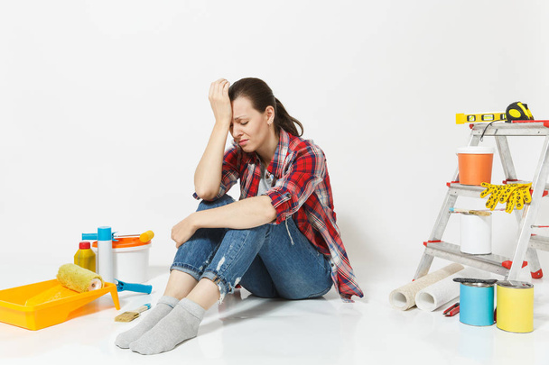 Confused annoyed tired sad upset woman sitting on floor with instruments for renovation apartment isolated on white background. Wallpaper, accessories for gluing painting tools. Concept of repair home - Фото, изображение