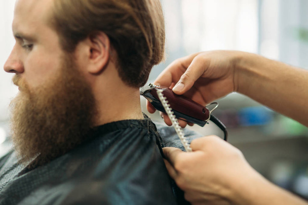 Бородатый мужчина стрижется с стрижкой для волос. Вид крупным планом с малой глубиной резкости
 - Фото, изображение