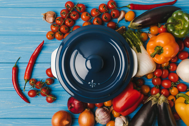 top view of pan between vegetables on blue table - Фото, изображение