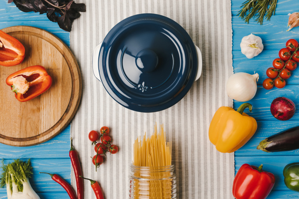 top view of pan and uncooked pasta with vegetables on blue table - Fotografie, Obrázek