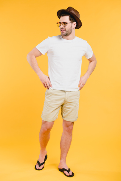 handsome young man in shorts and flip-flops smiling and looking away isolated on yellow - Foto, immagini
