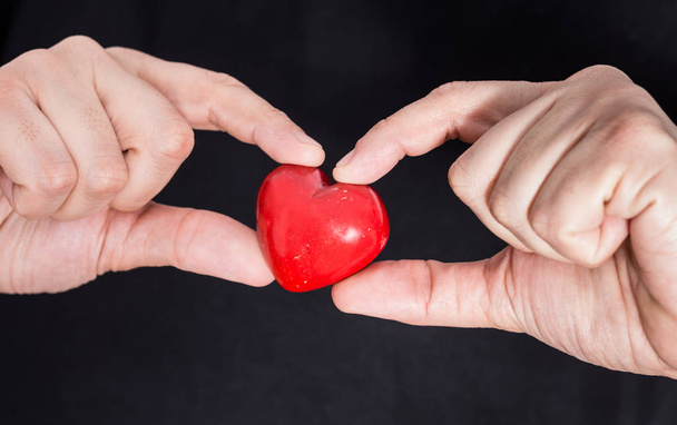 Αρσενικό χέρια που κρατούν closeup κόκκινη καρδιά, σε μαύρο φόντο. - Φωτογραφία, εικόνα