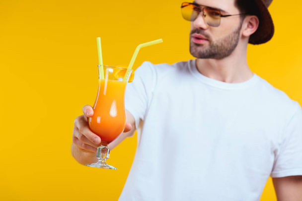 close-up view of bearded young man holding glass of summer cocktail isolated on yellow - Photo, Image