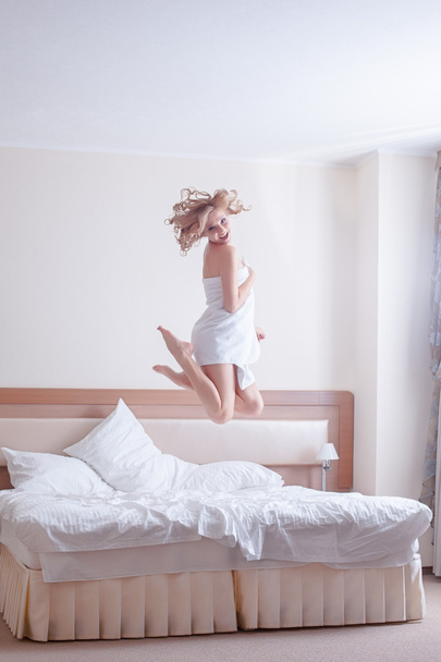 Happy young woman jumping on bed - Fotografie, Obrázek