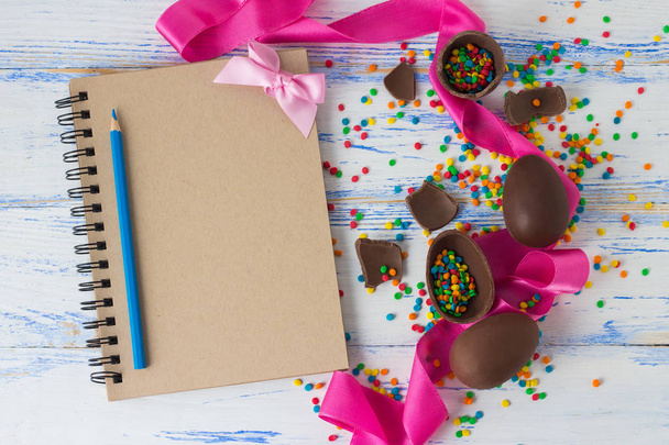 Huevos de chocolate de Pascua, cinta rosa, bloc de notas y lápices de colores
, - Foto, imagen