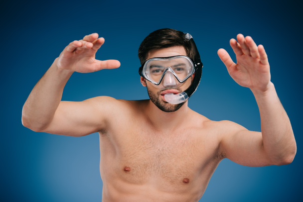 handsome shirtless young man in snorkel and diving mask swimming and looking at camera on blue  - Φωτογραφία, εικόνα