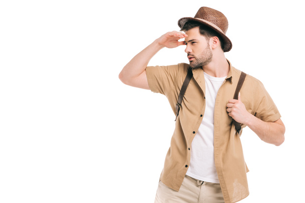 young traveler in hat holding backpack and looking away isolated on white - 写真・画像
