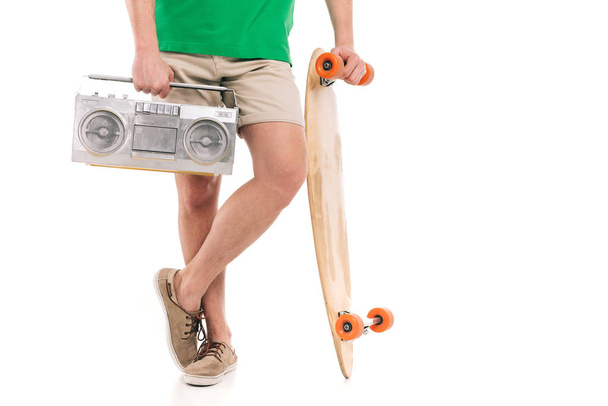 bijgesneden schot van jonge man in korte broek holding skateboard en tape recorder geïsoleerd op wit - Foto, afbeelding
