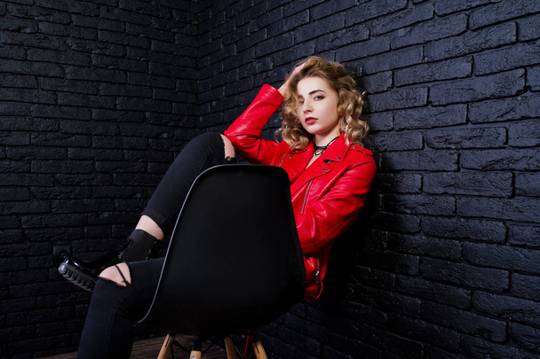 Studio portrait of blonde girl in red leather jacket posed on ch - Fotó, kép