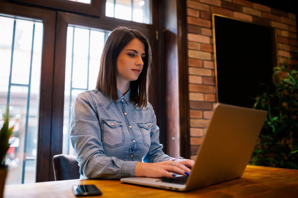 Escritora feminina sorridente trabalhando remotamente no dispositivo laptop conectando-se à internet sem fio.Freelancer feminino atraente com bom humor conversando em redes sociais com um amigo sentado na cafeteria
 - Foto, Imagem