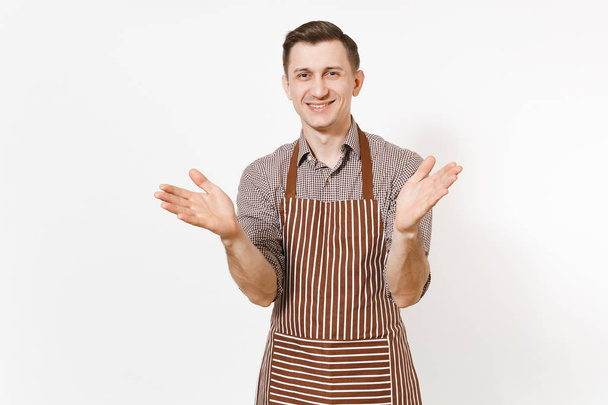 Young happy smiling man chef or waiter in striped brown apron, shirt stretching hands to camera isolated on white background. Male good housekeeper or houseworker. Domestic worker for advertisement. - Photo, Image