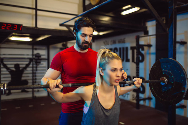 Young woman doing squat exercise at the gym with a personal trainer. - Photo, Image