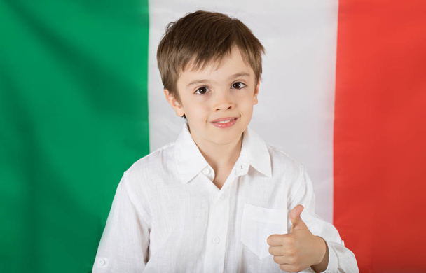 Lachende jongen van zeven jaar oud houdt een boek. Vlag van Italië als achtergrond. Closeup - Foto, afbeelding