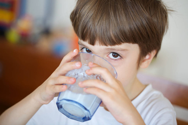 Jongen van zes jaar is het nemen van zijn ontbijt een glas warme melk met haver koekjes. Closeup - Foto, afbeelding