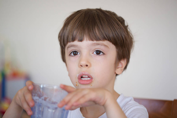 Kuusivuotias poika ottaa aamiaiseksi lasin lämmintä maitoa kaurakekseillä. lähikuva-analyysi
 - Valokuva, kuva