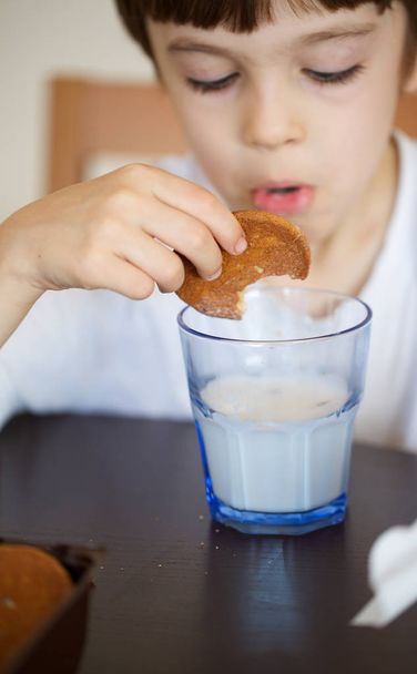 Kuusivuotias poika ottaa aamiaiseksi lasin lämmintä maitoa kaurakekseillä. lähikuva-analyysi
 - Valokuva, kuva