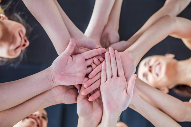 Закройте фотографию молодых улыбающихся женщин, поднимающих руки вместе. Друзья со стопкой рук демонстрируют единство и командную работу
. - Фото, изображение