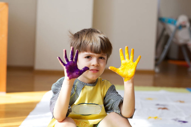 6-vuotias lapsi maalaa valkoista huopaa kämmenillään.
 - Valokuva, kuva