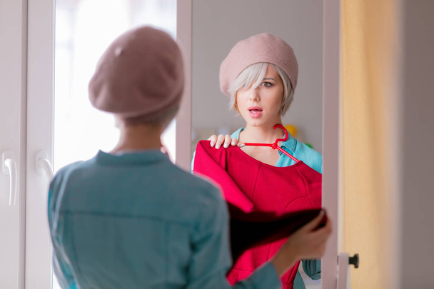 Jong meisje in baret met korte haren omhoog het kleden van nabij spiegel thuis - Foto, afbeelding
