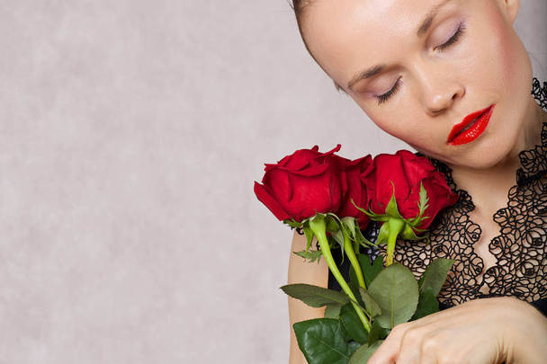 Young caucasian lady between 30 and 40 years old is posing in black blouse with red lipstick and red roses. Closeup  - Photo, Image