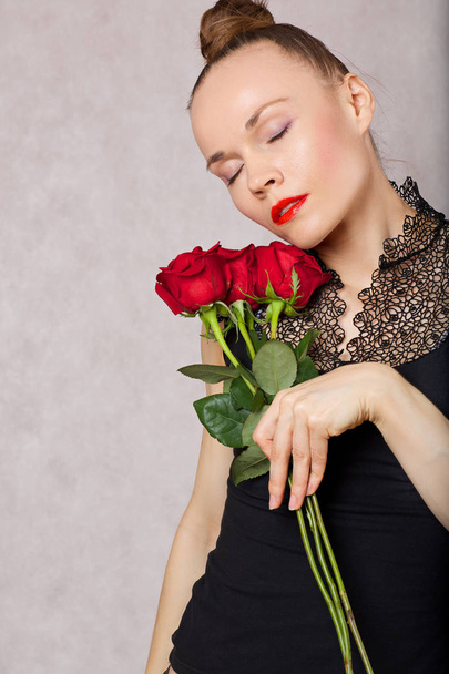 Young caucasian lady between 30 and 40 years old is posing in black blouse with red lipstick and red roses. Closeup  - Фото, зображення