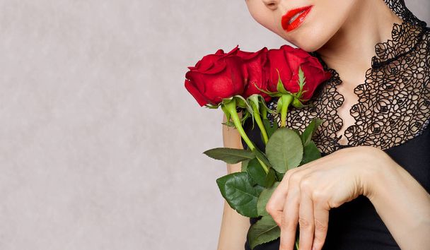 Молодая белая леди в возрасте от 30 до 40 лет позирует в черной блузке с красной помадой и красными розами. Крупный план
  - Фото, изображение