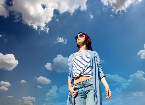 Young style redhead girl in modern clothes on blue sky with clouds background  - Foto, imagen