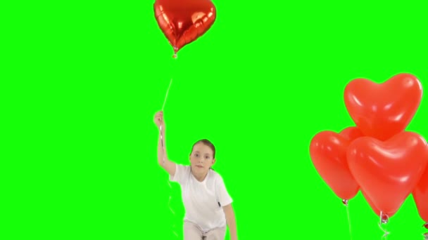Little girl holding bundle of red heart shaped air balloons. Bounces up. isolated on green screen. Slow-motion shooting - Footage, Video