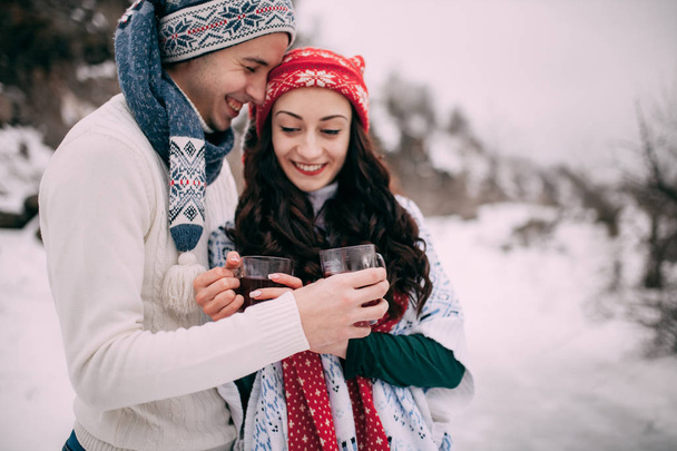 Portrain de pareja sonriente con tazas de té caliente en sus manos durante la caminata de invierno
. - Foto, Imagen