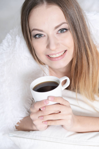  young beautiful woman with a cup of tea on sofa at home - 写真・画像