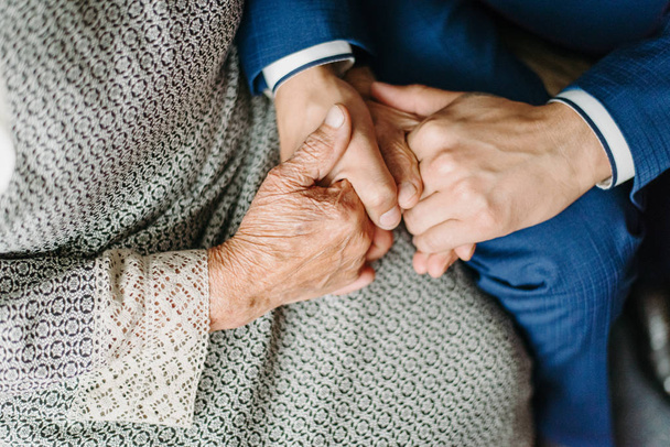 Закройте вид на руки пожилой женщины и молодого человека, держащихся вместе - Фото, изображение