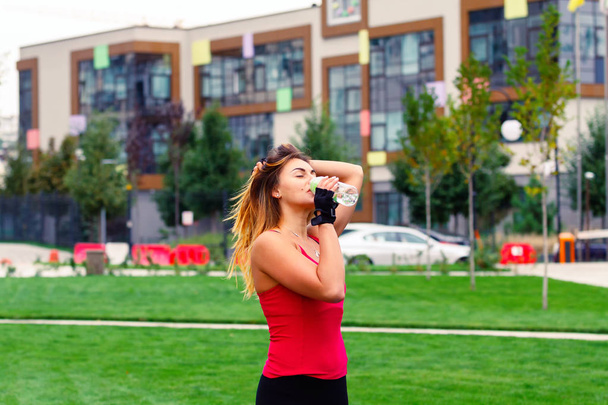 Mujer con ropa deportiva bebiendo agua después del entrenamiento en el paisaje de la ciudad
 - Foto, imagen