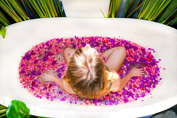 Rusovlasá dívka v koupelně s květina rim. Žena se uvolňuje v kulaté venkovní koupele tropické květiny, bio kosmetika, luxusní spa hotel Bali Ubud. Boční pohled s kopií prostor - Fotografie, Obrázek