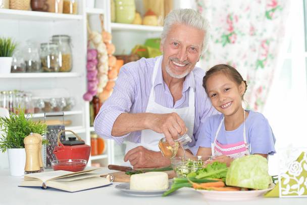 Senior man with granddaughter preparing dinner in kitchen - Foto, afbeelding