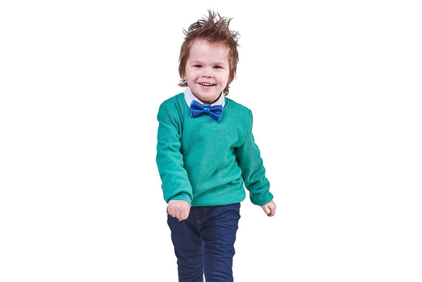 schöner kleiner Junge, mit blauer Fliege und grünem Pullover, spazierend und lächelnd, isoliert auf weißem Hintergrund - Foto, Bild