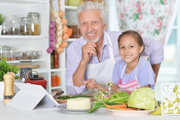 Senior man with granddaughter preparing dinner in kitchen - Fotó, kép