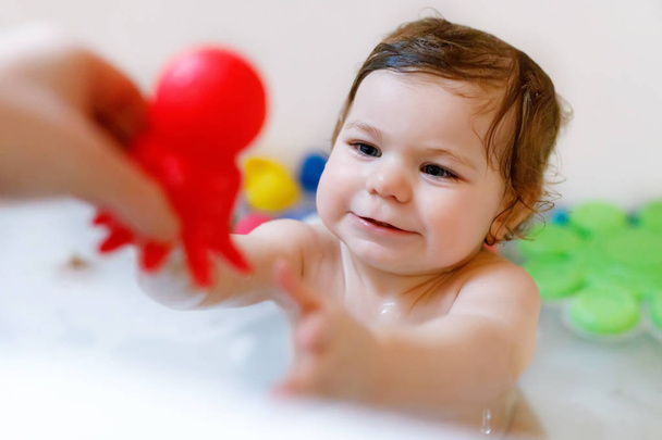 Cute adorable baby girl taking foamy bath in bathtub. Toddler playing with bath rubber toys. - Photo, Image