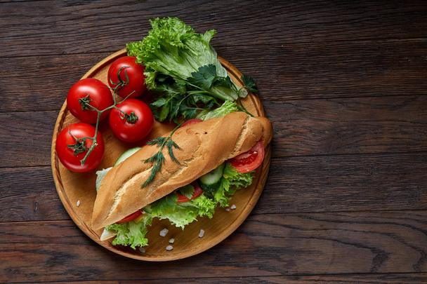 Fresh sandwich with lettuce, tomatoes, cheese on wooden plate, cup of coffee on rustic background, selective focus - Photo, image