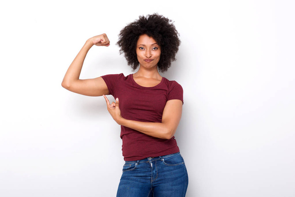 Portrait of fit young african woman pointing at arm muscles on white background - Фото, изображение