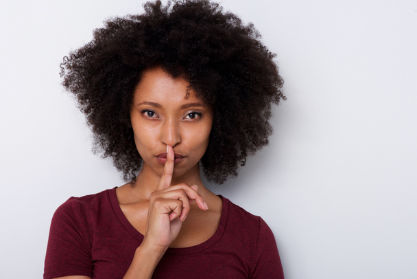 Retrato de cerca de una hermosa joven negra con el dedo sobre los labios haciendo gestos de silencio
 - Foto, Imagen